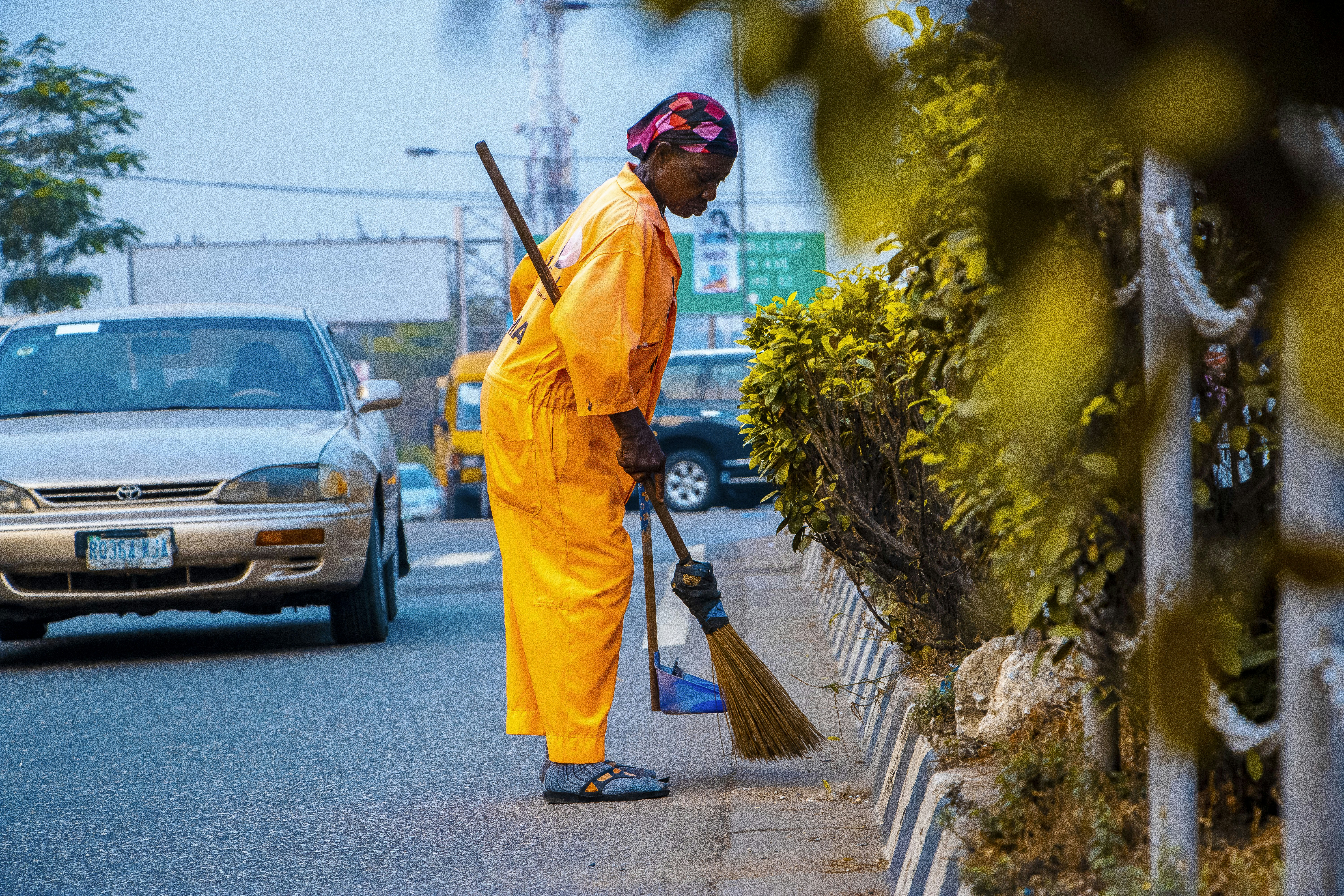 man in orange robe holding broom near parked cars during daytime