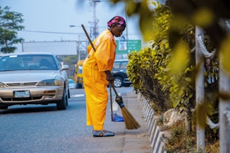man in orange robe holding broom near parked cars during daytime
