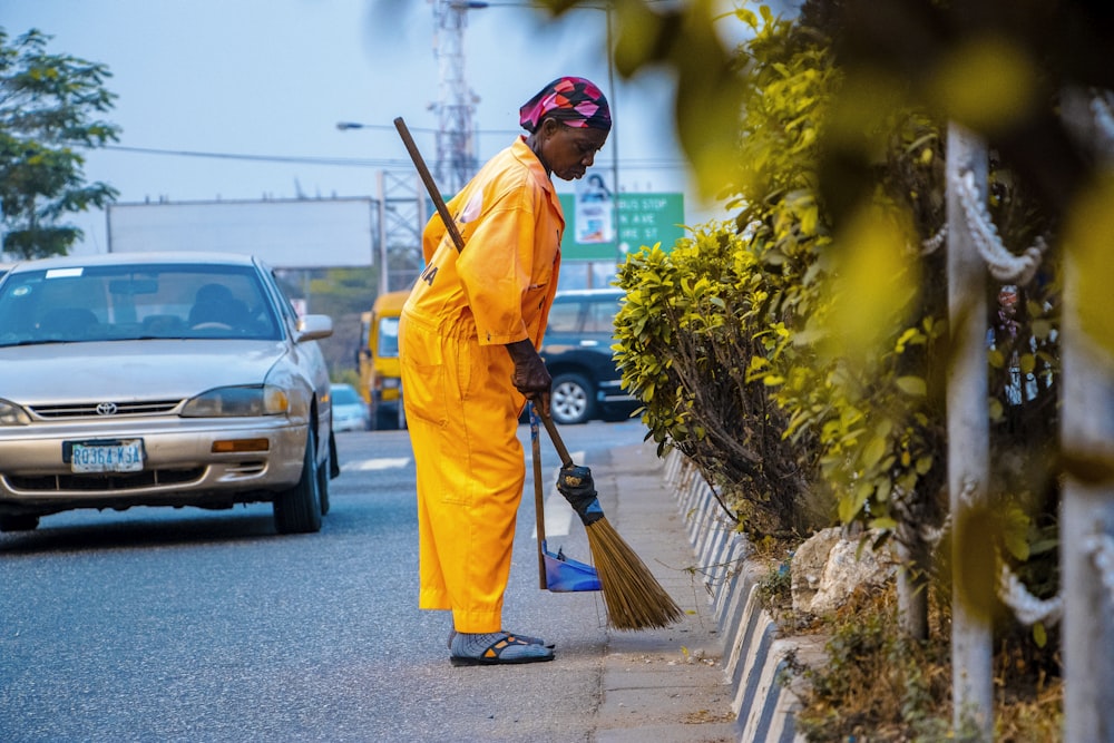 man in orange robe holding broom near parked cars during daytime