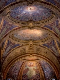 Intricate mosaic artwork adorns the domed ceiling, depicting religious figures and angels in vibrant colors. Latin script weaves through the golden arches, adding elegance to the sacred space.