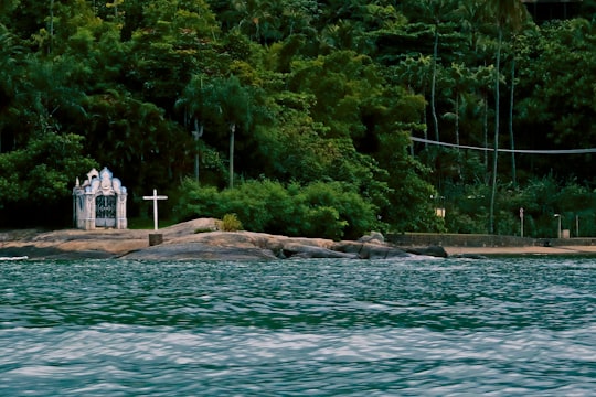 white and brown concrete building near green trees and body of water during daytime in Ilhabela Brasil