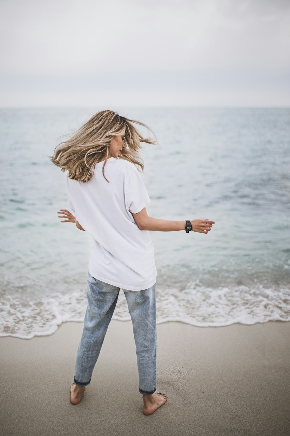 흰색 셔츠와 파란색 데님 청바지를 입은 여자가 낮 동안 해변 해변에 서 있다