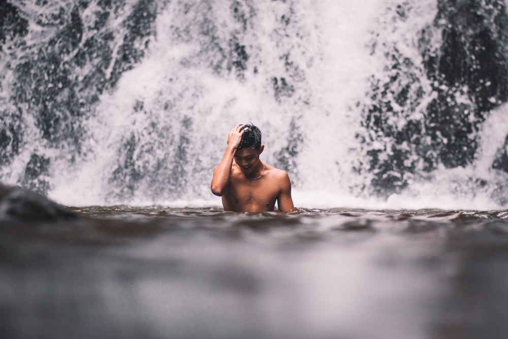 man in water falls during daytime