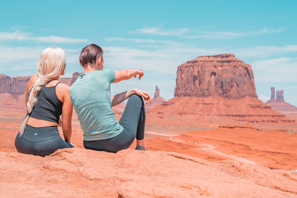 woman in teal tank top and black leggings sitting on brown rock formation during daytime