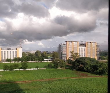A landscape with modern office buildings surrounded by lush greenery under a dramatic cloudy sky.