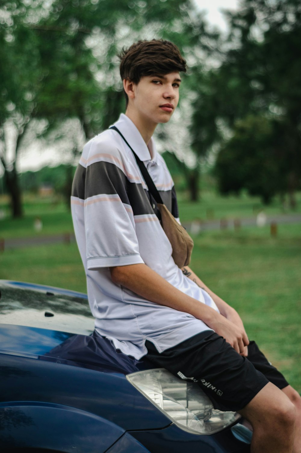 man in white and black polo shirt and black pants sitting on blue car hood during