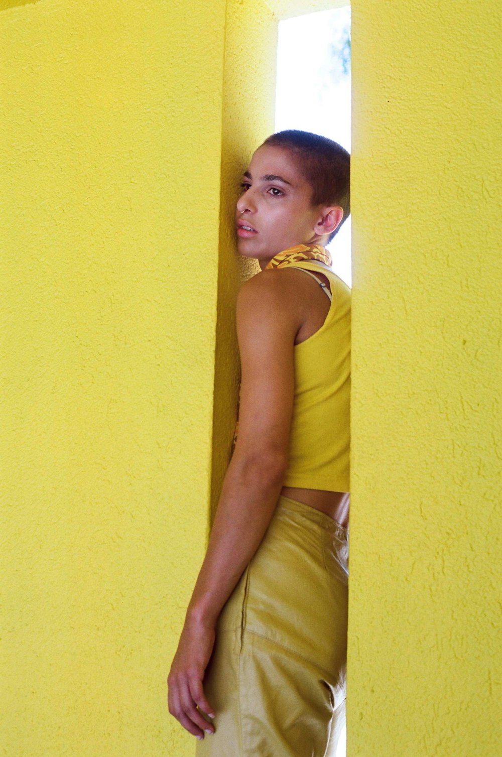 femme en débardeur jaune s’appuyant sur un mur jaune