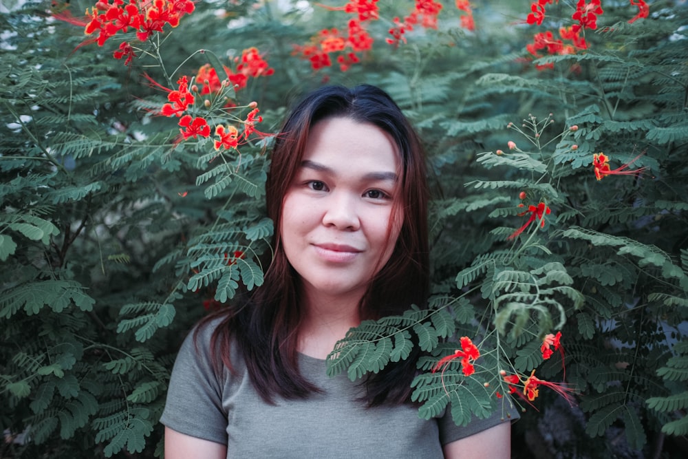 woman in gray crew neck t-shirt standing beside red flowers