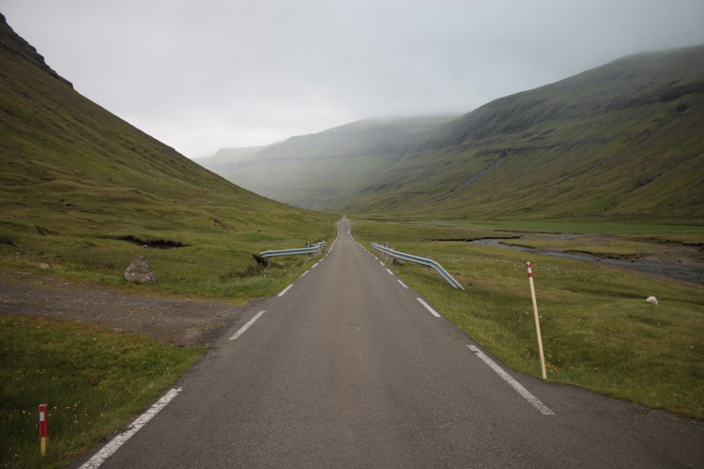 gray concrete road between green grass field near mountain during daytime