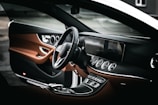 The interior of a luxury car features a sleek, modern dashboard with an integrated digital display and multiple air vents. The steering wheel has a stylish design with a prominent logo in the center. The upholstery combines dark and tan leather accents, contributing to an elegant and sophisticated atmosphere.
