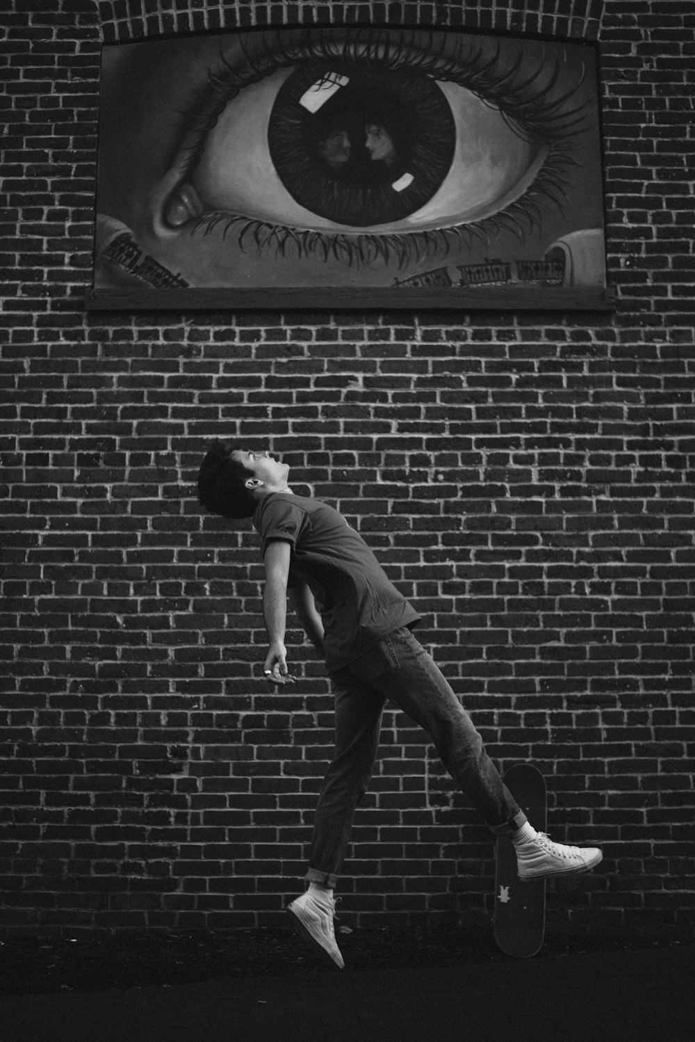 man in gray t-shirt and black pants leaning on brick wall