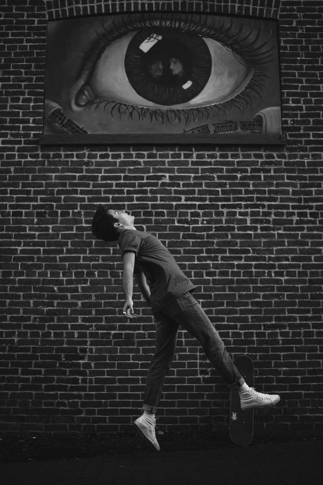 man in gray t-shirt and black pants leaning on brick wall