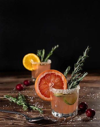 A vibrant cocktail glass garnished with fresh herbs and citrus on a wooden table with a Jura landscape background.