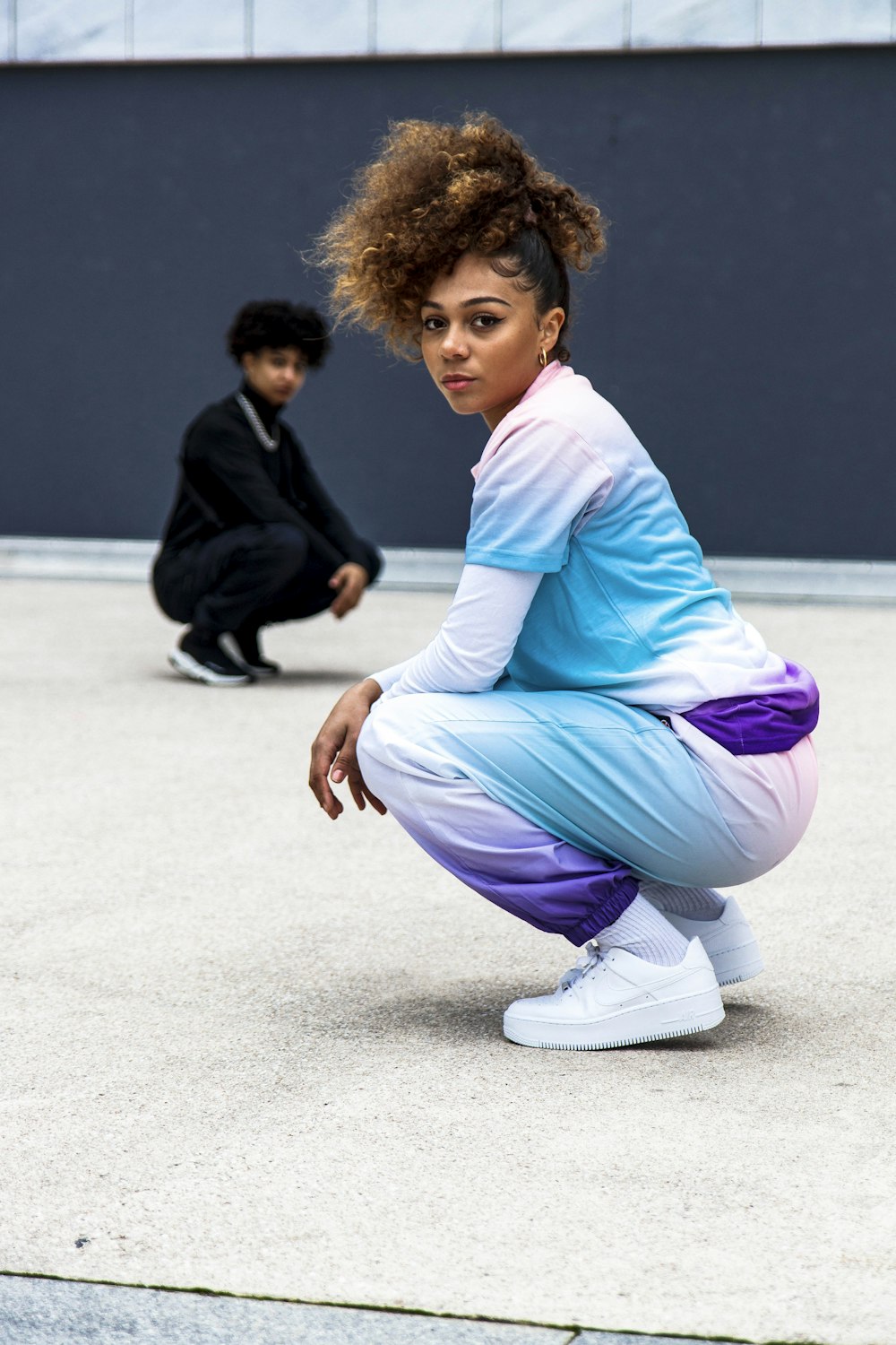 woman in white long sleeve shirt and purple pants sitting on gray concrete floor