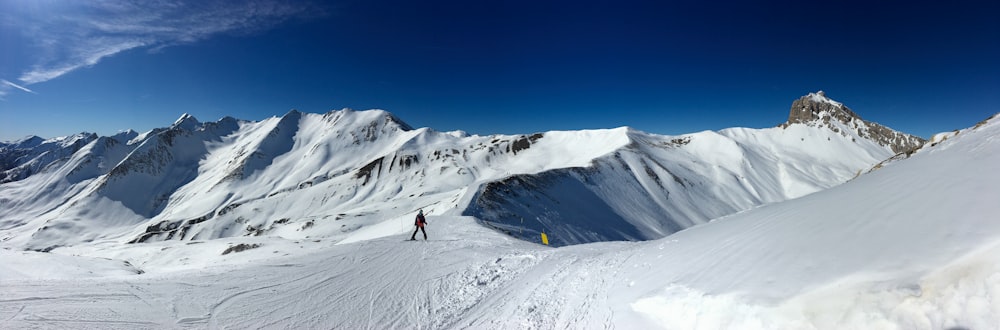 pessoa em jaqueta preta e calças azuis em pé na montanha coberta de neve durante o dia