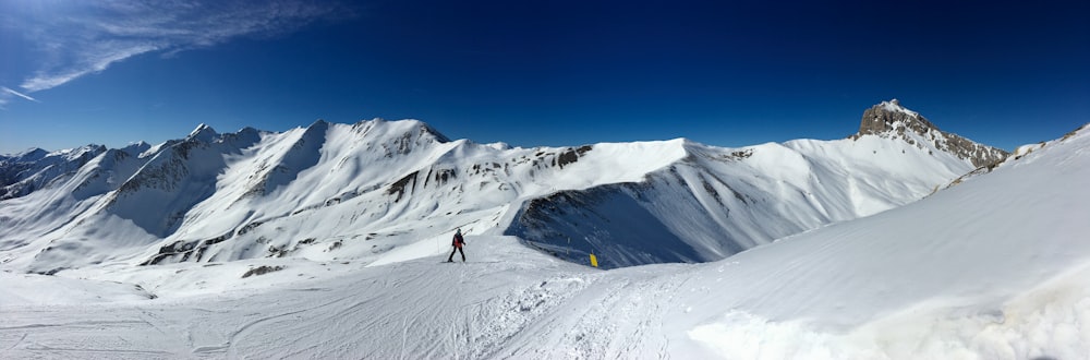 Person in schwarzer Jacke und blauer Hose, die tagsüber auf einem schneebedeckten Berg steht