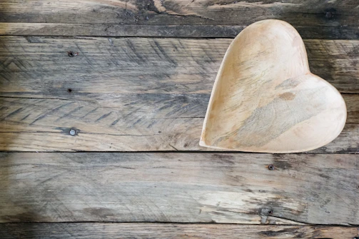 A rustic wooden bowl carved by tribal artisans, resting on a textured fabric background.