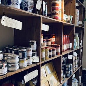 Selection of pantry staples including farine, riz, levure, and confitures in rustic containers.
