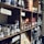 A wooden shelf filled with various jars, bottles, and packages of food products, including truffles, sauces, pasta, and preserved goods. Each shelf holds differently sized containers with labels and tags, creating a rustic and artisanal ambiance.