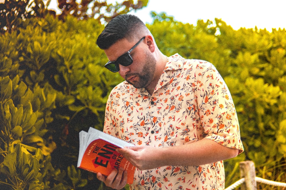 man in white and yellow floral button up shirt holding book