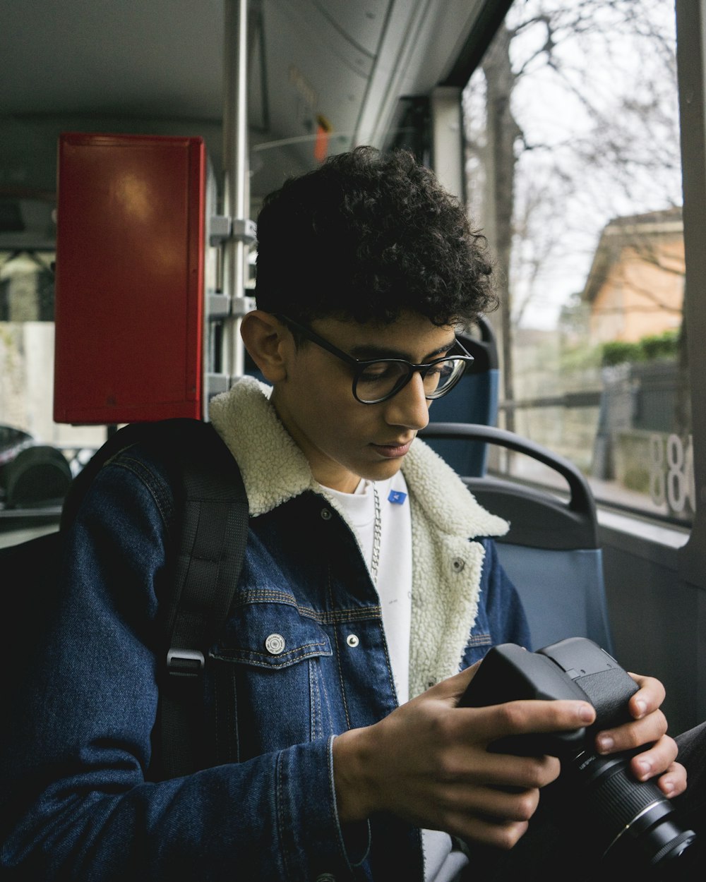 Mann in blauer Jeansjacke mit schwarz gerahmter Brille mit schwarzem Smartphone