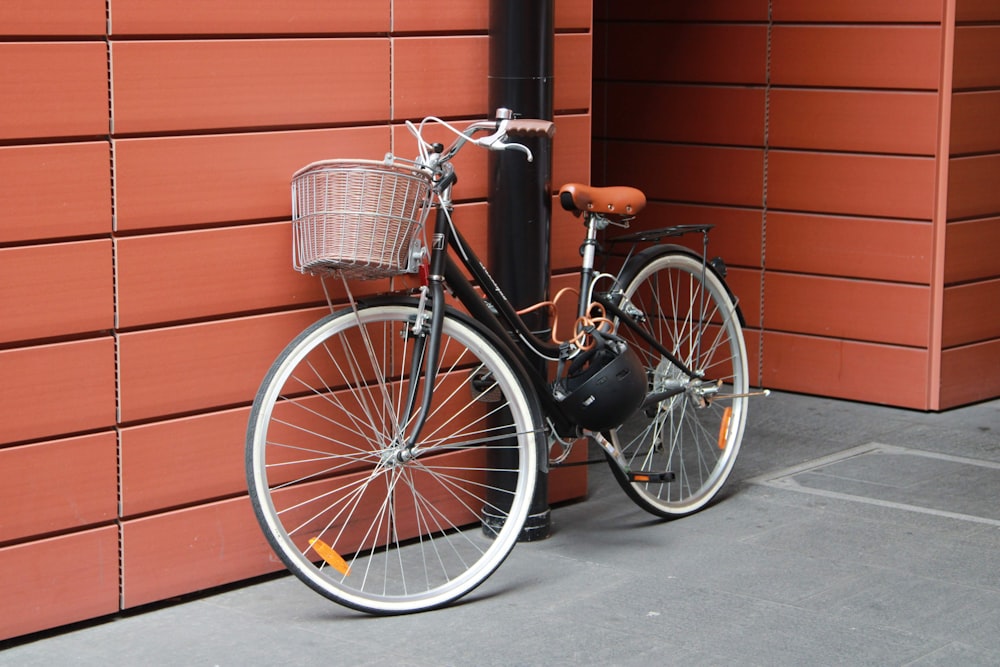 bicicleta da cidade preta estacionada ao lado da parede de tijolos vermelhos