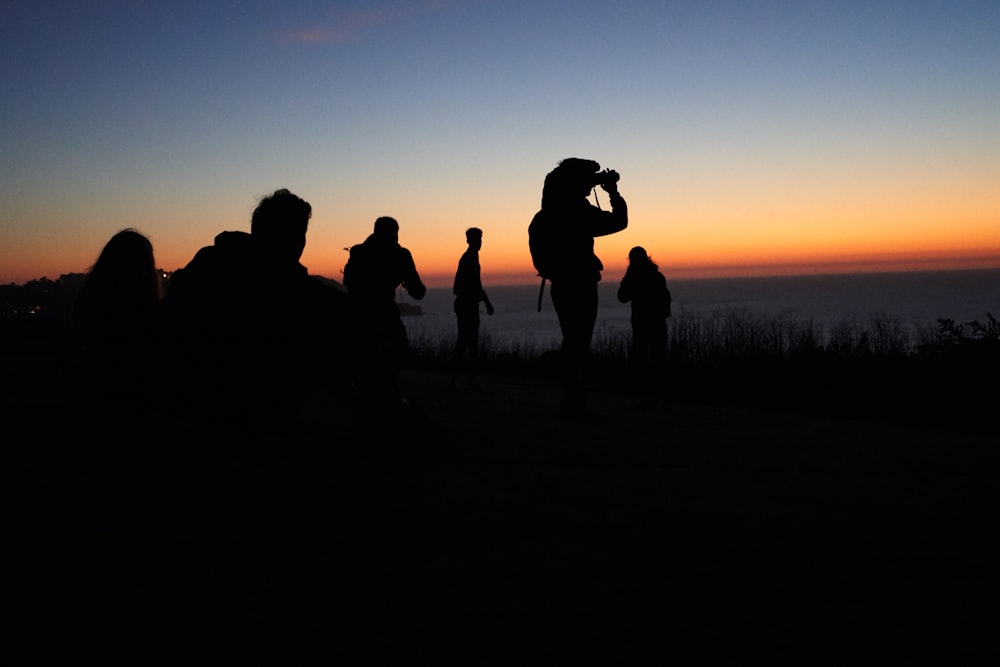 silhueta de pessoas em pé no campo de grama durante o pôr do sol