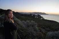 A confident woman traveler standing on a cliff overlooking a breathtaking coastal landscape.