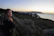 A smiling woman standing on a terrace overlooking the vibrant coastline at sunset.