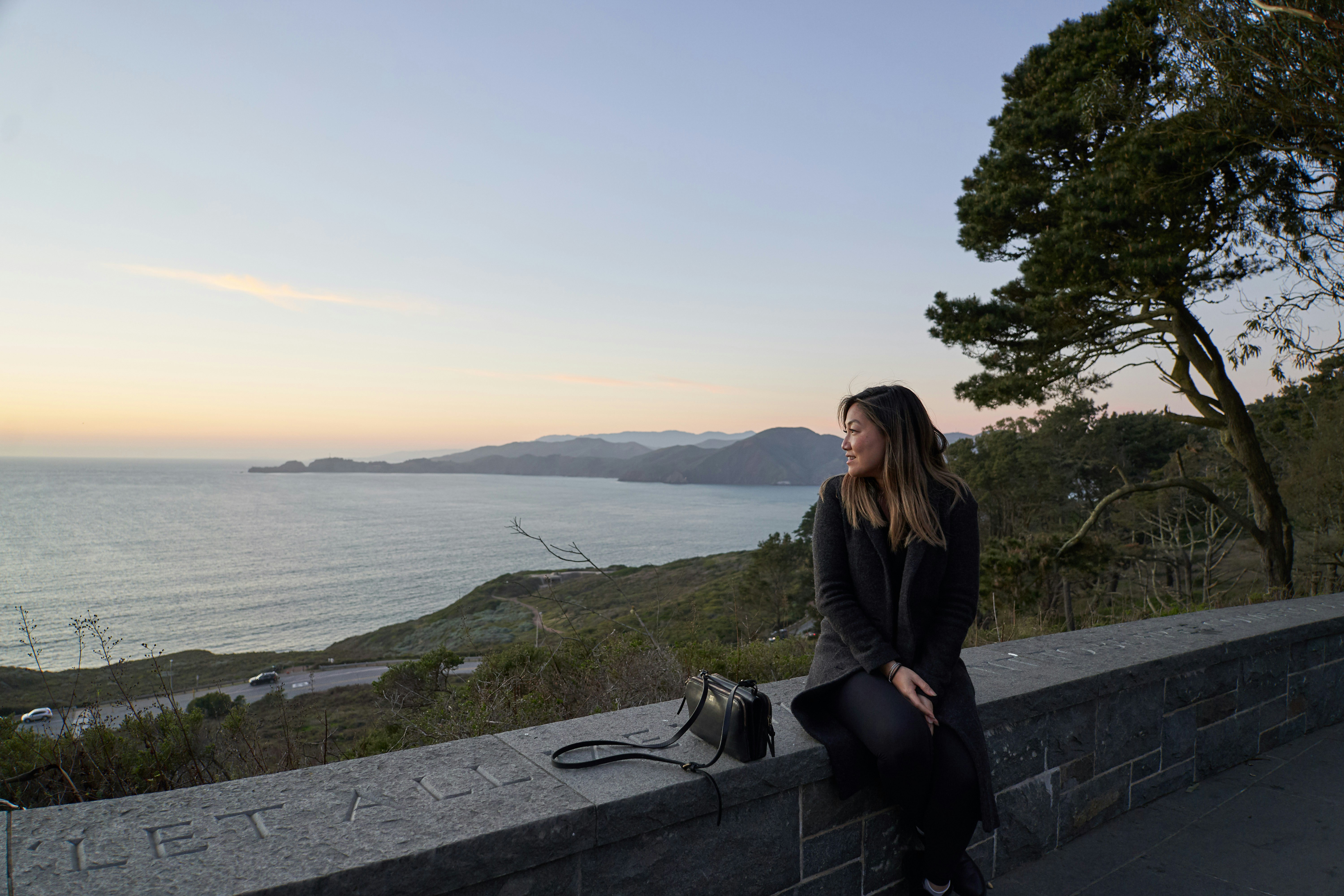 woman in black jacket sitting on gray concrete bench near body of water during daytime