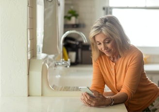 woman in orange long sleeve shirt using white smartphone