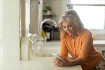 woman in orange long sleeve shirt using white smartphone