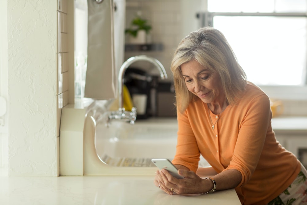 woman in orange long sleeve shirt using white smartphone
