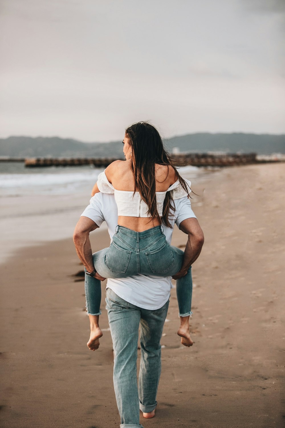 woman in white shirt and blue denim jeans standing on beach during daytime