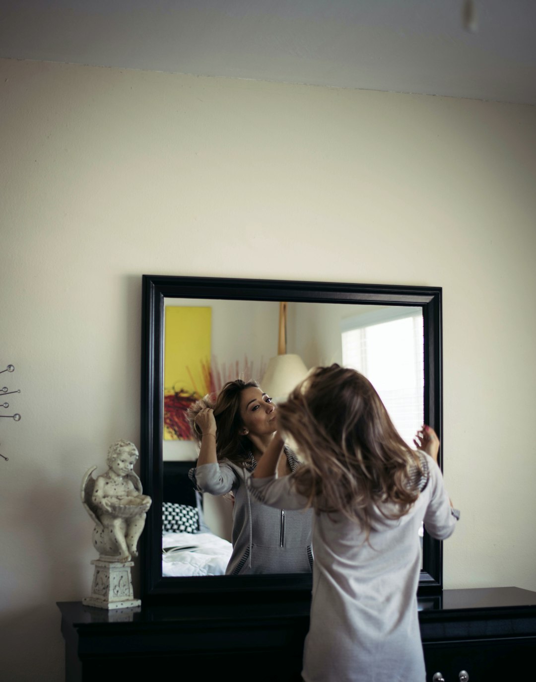 woman in white long sleeve shirt standing beside black framed mirror