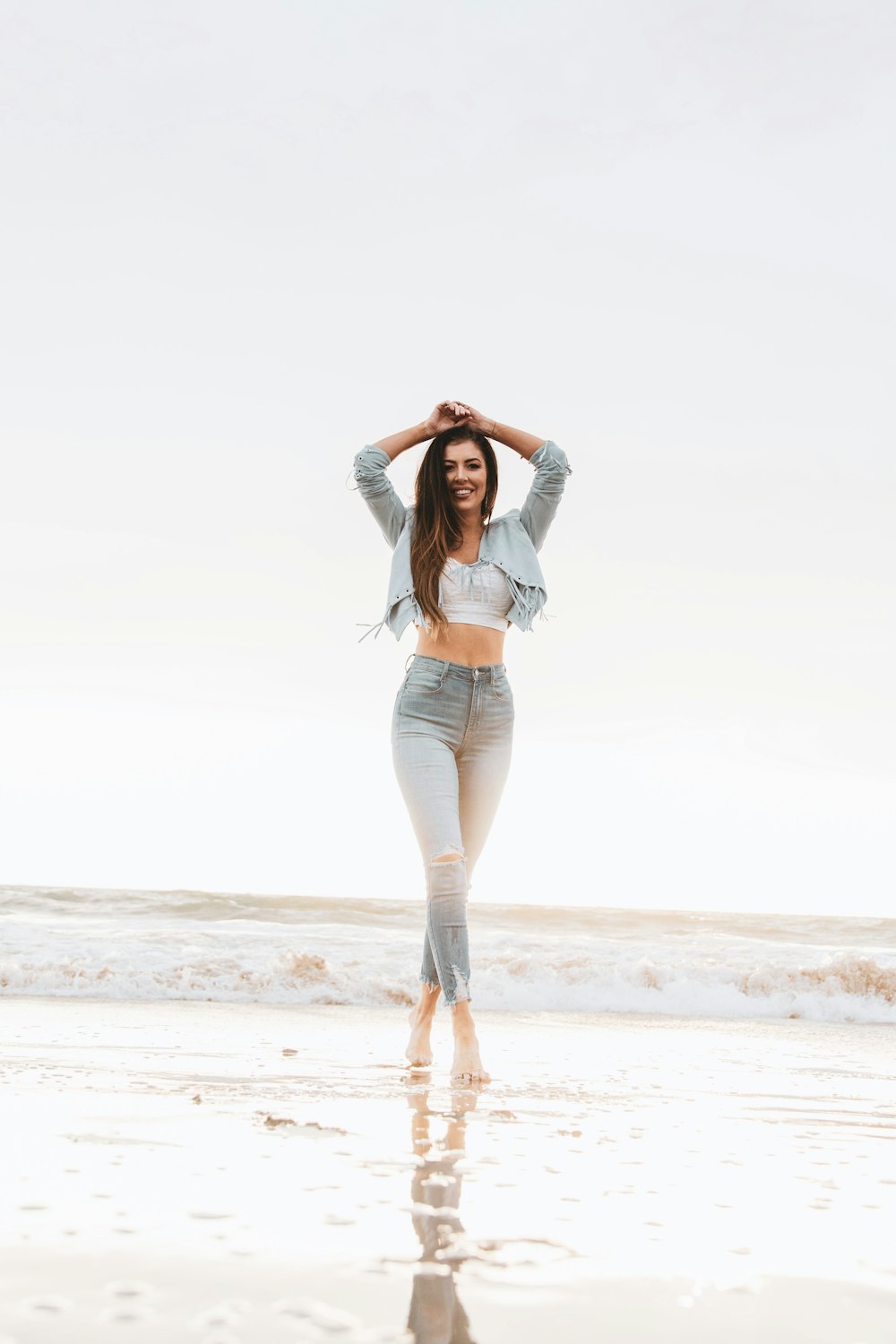 woman in blue denim jacket and blue denim jeans standing on beach shore during daytime