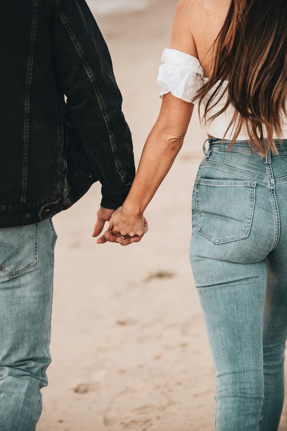 woman in white shirt and blue denim jeans holding hands with man in blue denim jeans