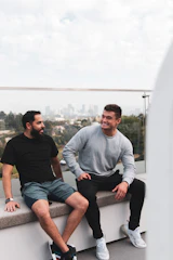 A candid photo of two men in conversation, smiling with a blurred cityscape background