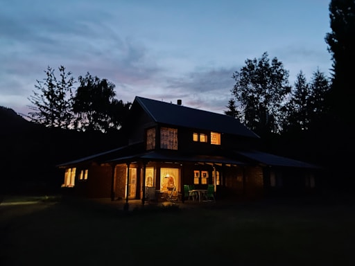 Cozy rustic house exterior at sunset with warm lights glowing from windows