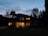 A cozy custom-built home with warm lighting glowing through large windows at dusk.