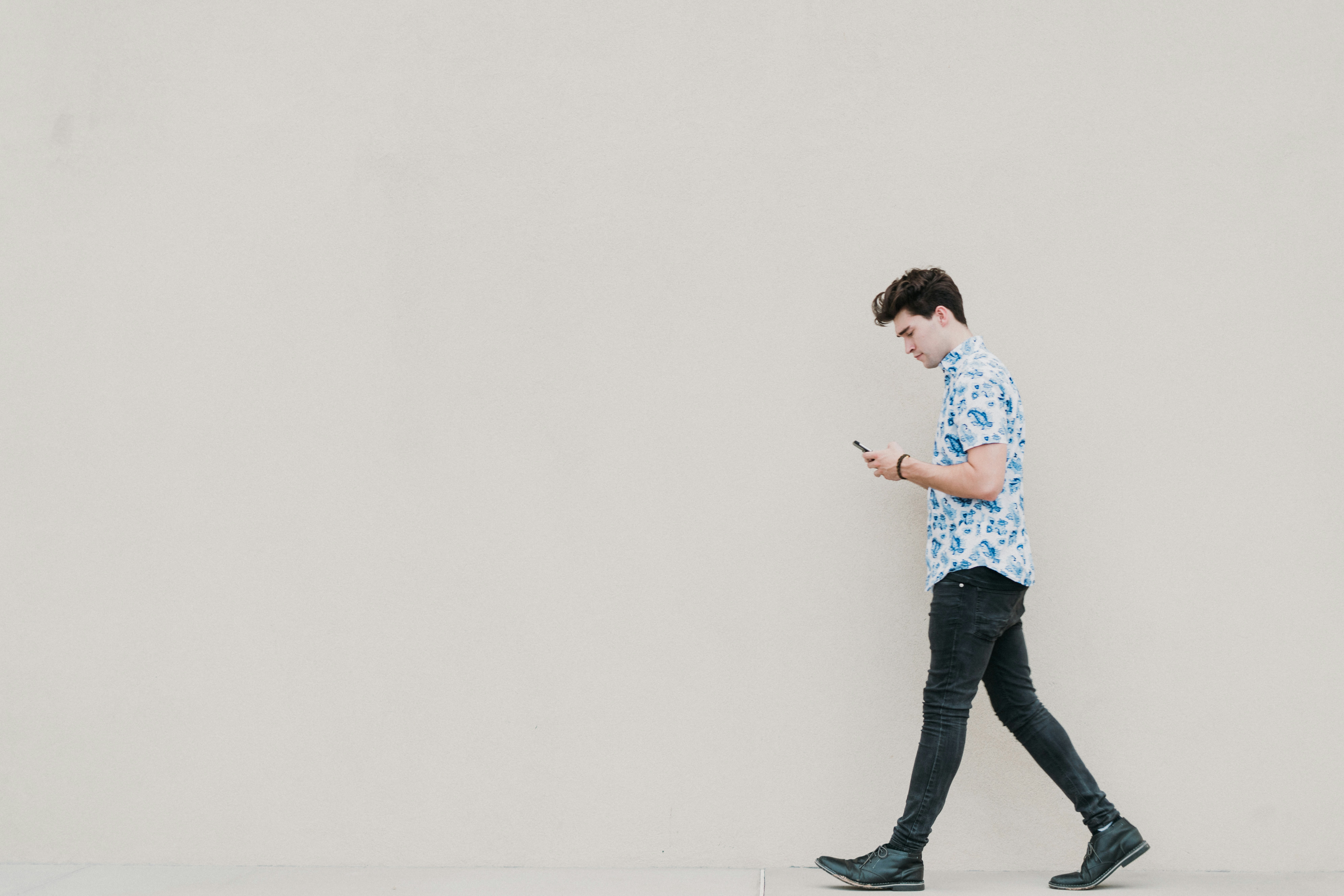 man in blue and white floral dress shirt and black pants standing on white wall