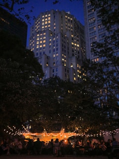 A lively outdoor summer gala with members mingling under string lights at dusk