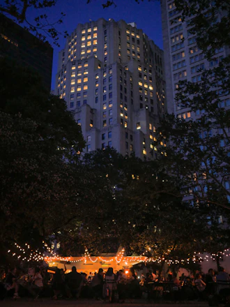 A lively crowd enjoying a spring evening gala with string lights and floral decorations.