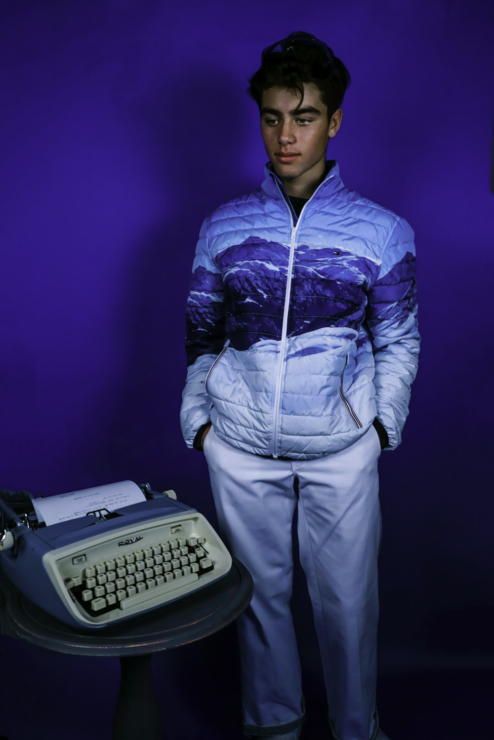 man in blue zip up jacket and white pants standing beside white typewriter