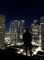 Silhouette of a podcaster wearing headphones against a city skyline at night.