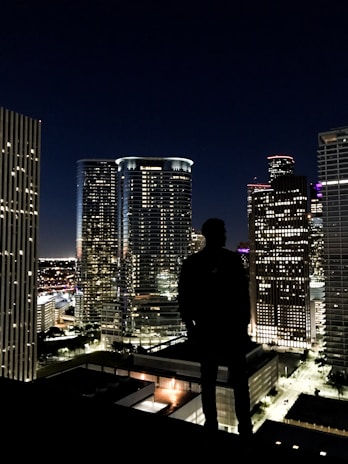 Shadowed silhouette of a detective observing a cityscape at night.