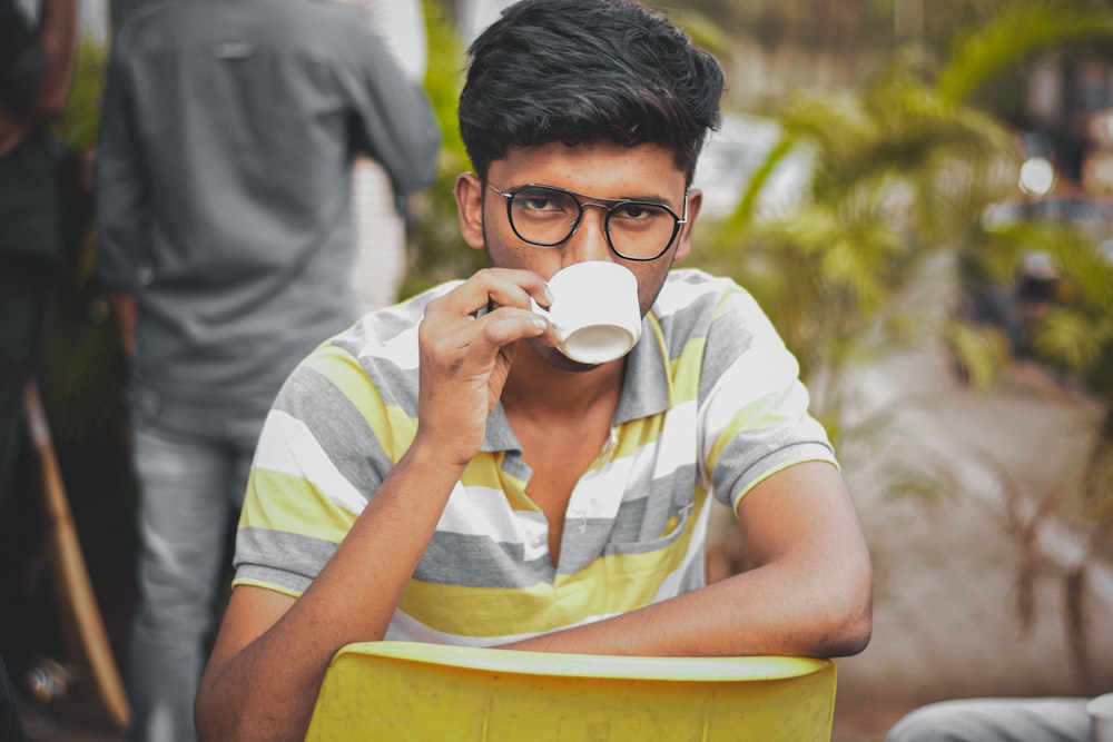 man in white and yellow stripe polo shirt drinking from white ceramic mug