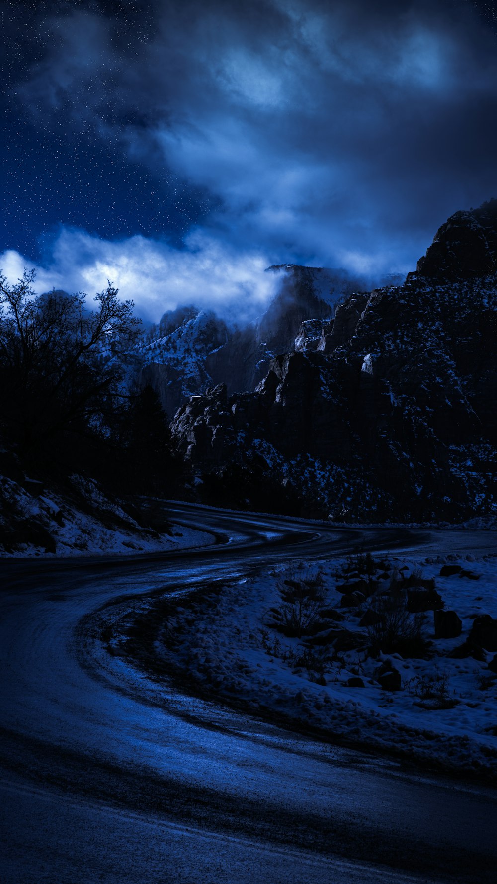 strada innevata vicino agli alberi e alla montagna sotto il cielo nuvoloso durante il giorno