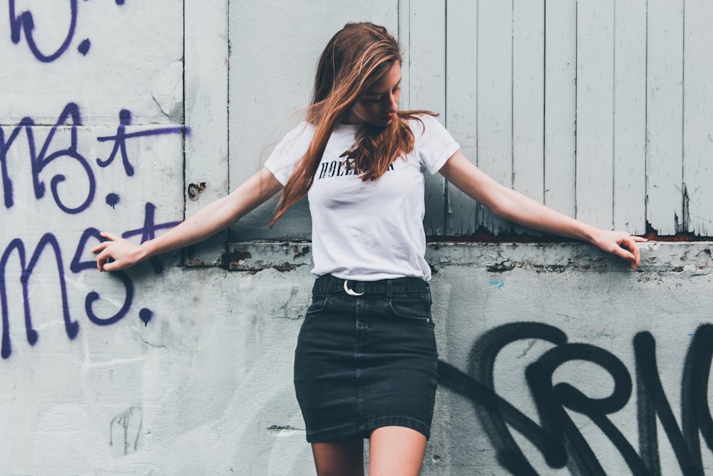 woman in white shirt and black skirt standing beside wall
