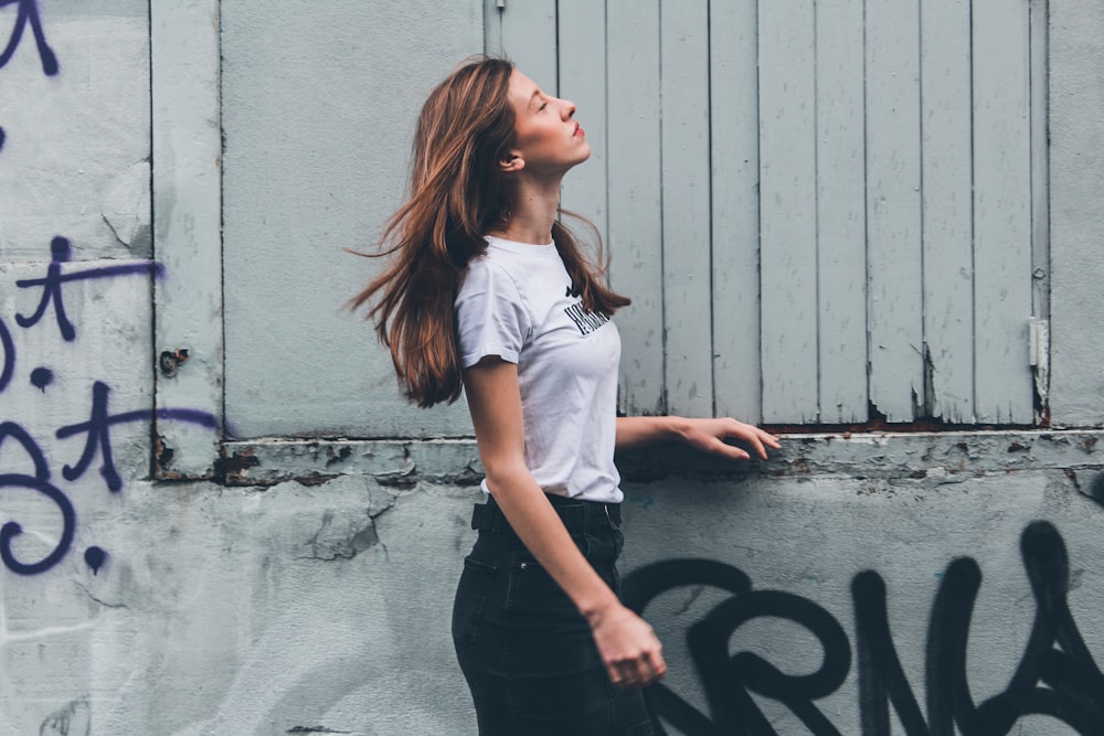 woman in white t-shirt and black pants leaning on wall